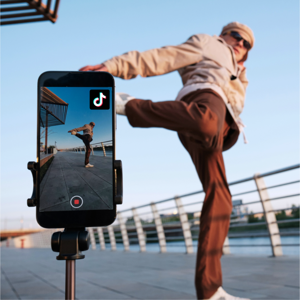 Junge Person führt einen Kick aus, während sie von einem Smartphone mit TikTok-Logo gefilmt wird.